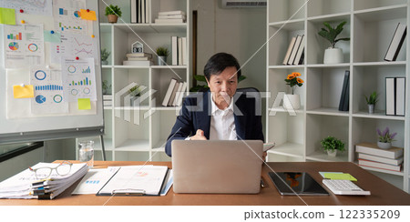 Elderly businessman presenting data insights while working on a laptop in a modern office 122335209