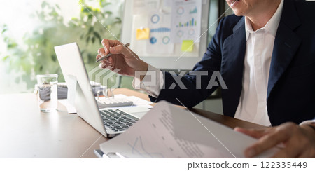 Elderly businessman discussing data insights while reviewing reports in a modern office 122335449