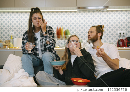 A group of friends joyfully enjoying delicious snacks together in the comfort of home A group of friends joyfully enjoying delicious snacks together in the comfort of home 122336756