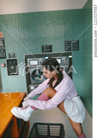 A young woman is tying her shoelaces in a chic and stylish laundry room environment A young woman is tying her shoelaces in a chic and stylish laundry room environment 122337087