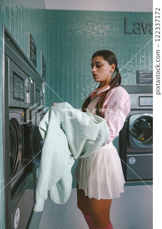 A Fashionable and Stylish Young Woman at a Bright Laundromat Wearing a Cozy Pastel Sweater 122337172