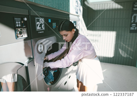 A young woman expertly using a laundry machine in a contemporary, modern laundromat setting 122337187