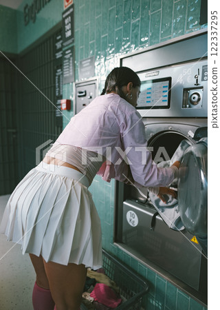 A young woman at a laundromat dressed in a stylish outfit while doing her laundry A young woman at a laundromat dressed in a stylish outfit while doing her laundry 122337295