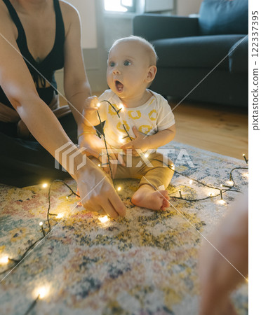 A Sweet Baby Joyfully Playing with Twinkling Christmas Lights in a Cozy Home Setting A Sweet Baby Joyfully Playing with Twinkling Christmas Lights in a Cozy Home Setting 122337395