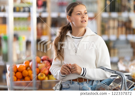 Portrait of girl shopper with a shopping cart choosing some products in supermarket Portrait of girl shopper with a shopping cart choosing some products in supermarket 122337872