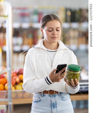 Woman scanning a jar of olives on her phone Woman scanning a jar of olives on her phone 122337932