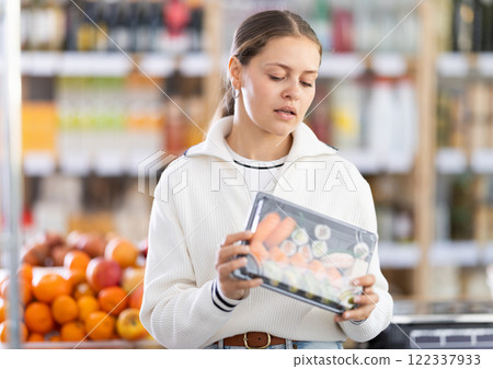 Choose food in supermarket - woman chooses japanese sushi to buy in the grocery department section of store 122337933