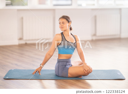 Young woman practicing parivritta sukhasana yoga pose 122338124