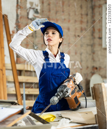 Female builder confidently holding pneumatic jackhammer in house under construction 122338303
