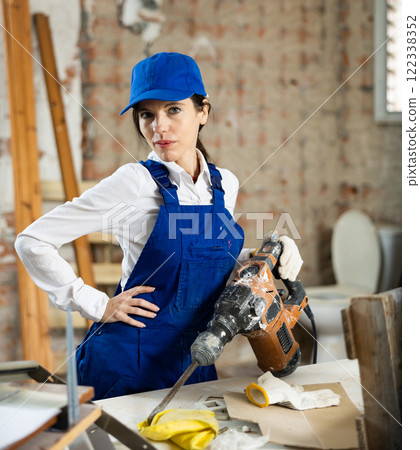 Female contractor standing with demolition hammer inside building under construction Female contractor standing with demolition hammer inside building under construction 122338352