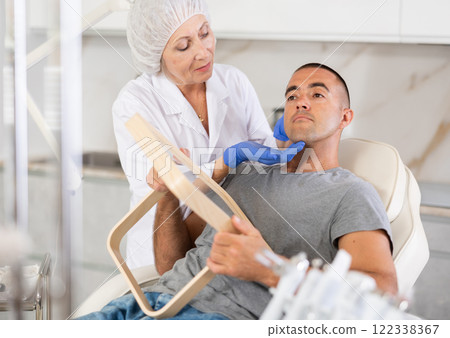 Female doctor, together with male patient, examines face in mirror after undergoing hardware procedure for skin rejuvenation Female doctor, together with male patient, examines face in mirror after undergoing hardware procedure for skin rejuvenation 122338367