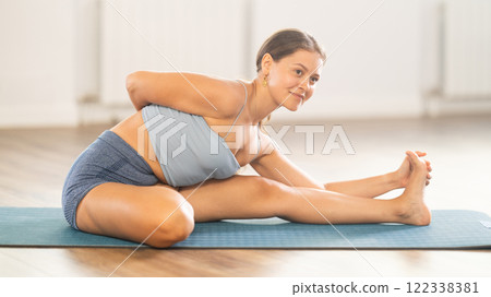 Sportive girl practicing head to knee pose of yoga in light room 122338381