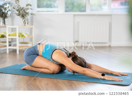 Sportive girl practicing child pose of yoga in light room 122338465