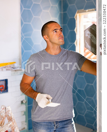 Focused man wearing ordinary clothes installing ceramic tiles whith construction trowel Focused man wearing ordinary clothes installing ceramic tiles whith construction trowel 122338472
