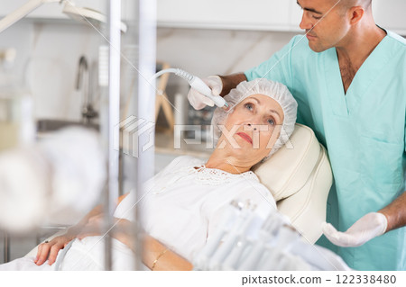 Male dermatologist performing cosmetology procedure for elderly woman, RF lifting and deep hydration for facial skin therapy 122338480