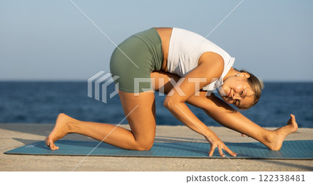 On windy day young slender woman does yoga near sea doing practicing hatha yoga 122338481