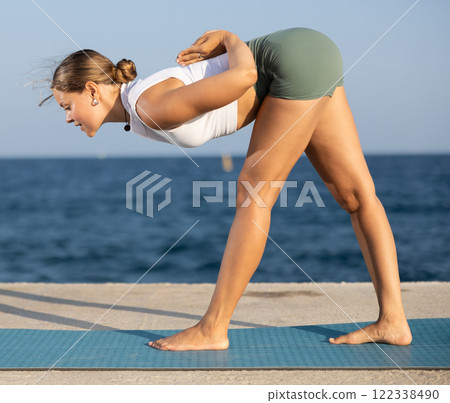 Athletic girl meditates in a yoga pose parshvottanasana on seashore Athletic girl meditates in a yoga pose parshvottanasana on seashore 122338490