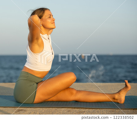 On windy day young slender woman does yoga near sea doing practicing hatha yoga On windy day young slender woman does yoga near sea doing practicing hatha yoga 122338502