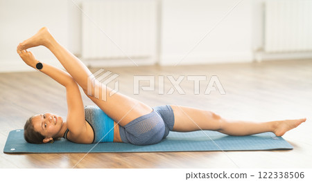 Sportive girl practicing reclining hand to toe pose of yoga in light room Sportive girl practicing reclining hand to toe pose of yoga in light room 122338506