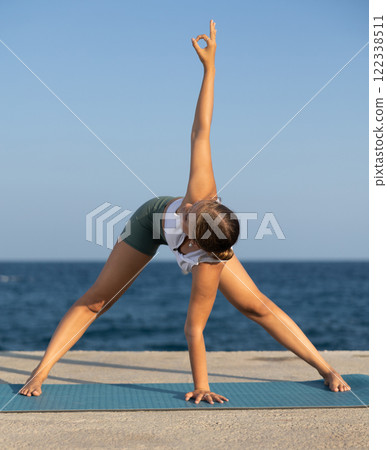 On windy day young slender woman does yoga near sea doing Himavanasana 122338511