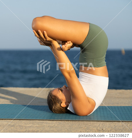 Athletic girl practicing reverse lotus pose on seashore Athletic girl practicing reverse lotus pose on seashore 122338627