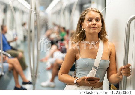 Young woman is standing in subway car with phone, getting to work school. Young woman is standing in subway car with phone, getting to work school. 122338631