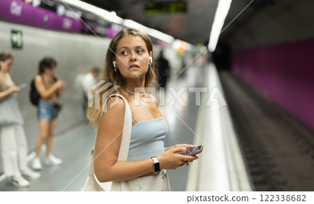Girl with earphones and phone is standing on subway platform 122338682