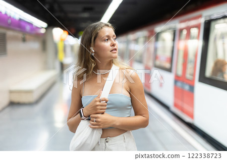 Girl with earphones is standing on subway platform, waiting for train to arrive Girl with earphones is standing on subway platform, waiting for train to arrive 122338723