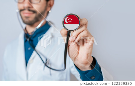 Doctor holding stethoscope with Singapore flag. Singapore Health and Care Concept, Singapore flag on stethoscope 122339380