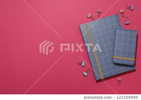 Two notebooks with paper clips on a burgundy background 122339499