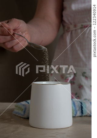 women's hands pour yeast into a mug of tea spoon 122340914