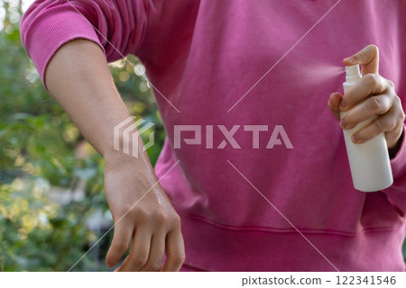 Person spraying insect repellent at her hand outdoors during summer. Trying to kill mosquitoes and flies. Clearly visible spray droplets. Prevention disinfection against mosquito bite 122341546