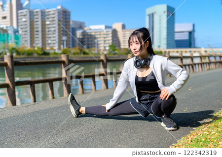 一個酷女人在河邊的人行道上伸展雙腿，散步，節食，散步，運動。 122342319