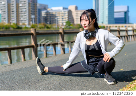 一個酷女人在河邊的人行道上伸展雙腿，散步，節食，散步，鍛煉，修剪。 122342320
