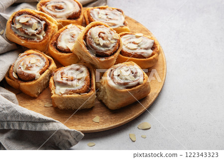 Delicious cinnamon rolls with white icing and almond flakes resting on wooden plate 122343323