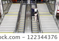 People ascending an escalator in a modern railway station. Bright, spacious public space with polished metal railings, organized infrastructure, and bustling transit movement. 122344376