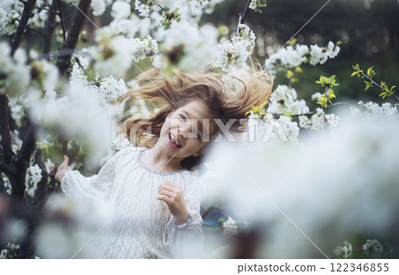 Laughing young girl dancing in the middle of blooming flowers. Concept of springtime in nature. 122346855