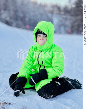 litte boy in neon green overall sitting on snow outside litte boy in neon green overall sitting on snow outside 122347488