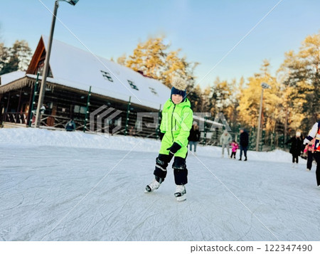 little boy in winter neon green overall skating on rink little boy in winter neon green overall skating on rink 122347490