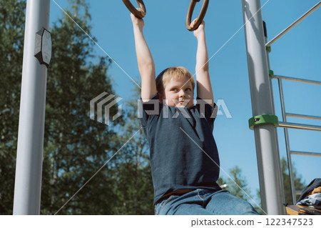 boy pull-up on rings at outdoor sportsground boy pull-up on rings at outdoor sportsground 122347523
