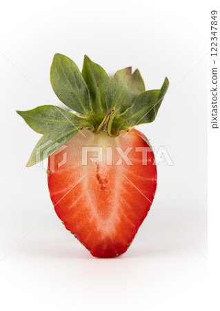 close up on white photo background there is a cut half of a ripe strawberry suspended in the air healthy vitamins seasonal summer fruit vitamin C green strawberry tail like a crown close up on white photo background there is a cut half of a ripe strawberry suspended in the air healthy vitamins seasonal summer fruit vitamin C green strawberry tail like a crown 122347849