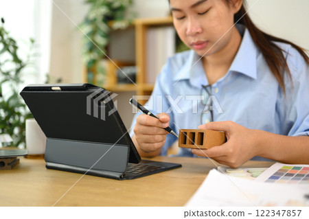 Female interior designer sitting in a cozy studio focuses on selecting materials for design project 122347857