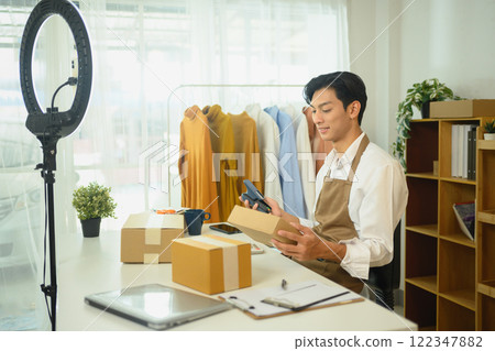 Young business owner in apron preparing packages for shipment in his home office Young business owner in apron preparing packages for shipment in his home office 122347882