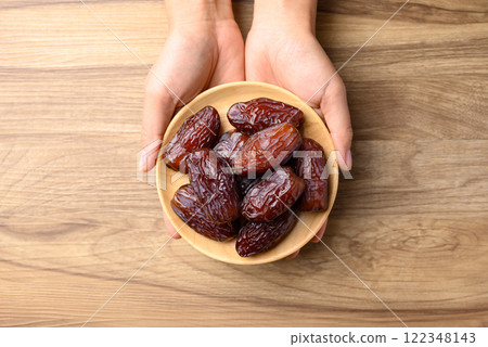 Date palm fruit (MedJool) on wooden plate holding by hand, Table top view 122348143