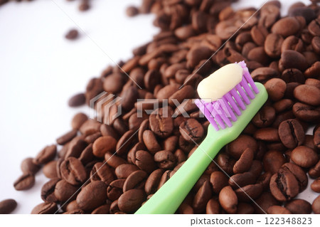 A green toothbrush with purple bristles and a dollop of white toothpaste rests diagonally on a pile of roasted coffee beans, emphasizing the contrast between dental care and coffee culture. A green toothbrush with purple bristles and a dollop of white toothpaste rests diagonally on a pile of roasted coffee beans, emphasizing the contrast between dental care and coffee culture. 122348823