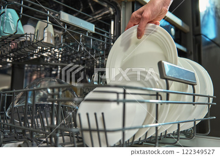 Woman unloading clean white plates from the bottom rack of dishwasher in kitchen. Person performing everyday household chores, using modern home appliance 122349527