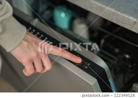 Hand pressing start button on dishwasher control panel with open door. Woman using modern home appliance, choosing automatic program on built in dishwasher for cleaning dirty dishes Hand pressing start button on dishwasher control panel with open door. Woman using modern home appliance, choosing automatic program on built in dishwasher for cleaning dirty dishes 122349528