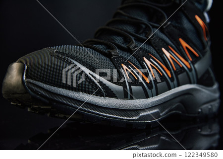 Close-up of waterproof black hiking boot with orange accents. Rugged trekking shoe on dark background. Footwear for exploration and outdoor activities Close-up of waterproof black hiking boot with orange accents. Rugged trekking shoe on dark background. Footwear for exploration and outdoor activities 122349580