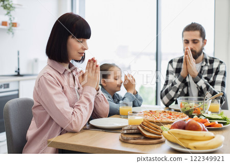 Caucasian family including mother, father, and daughter praying before breakfast. Seen in modern kitchen, focused on faith and gratitude. Represents harmony and family bonding. 122349921