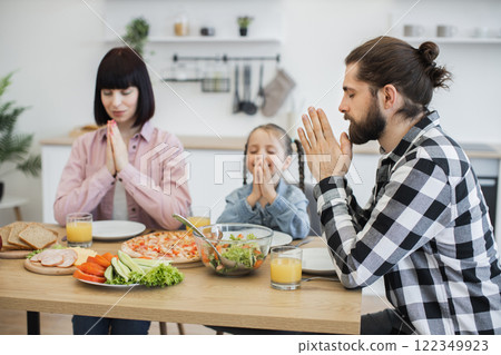 Caucasian family with parents and child praying before breakfast. Focus on togetherness, spirituality, and gratitude over healthy meal. Child around seven years old. 122349923